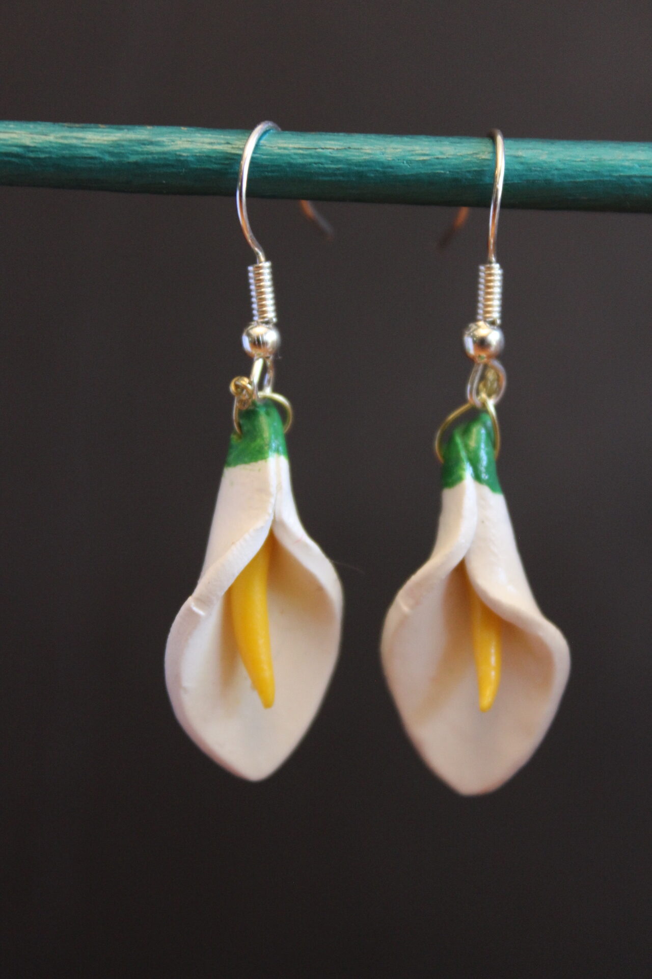 An example of the calla lily earrings is displayed, hanging from a bar, so customers can se how the earrings look while dangling as they would when worn.